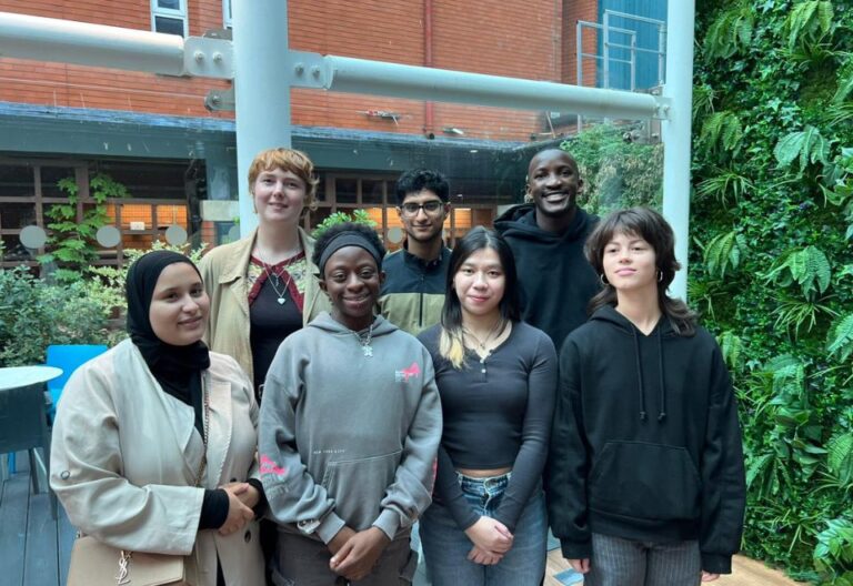 The Future Generations Panel - seven young people aged 18 to 25. Stood in a line in front of a leafy background
