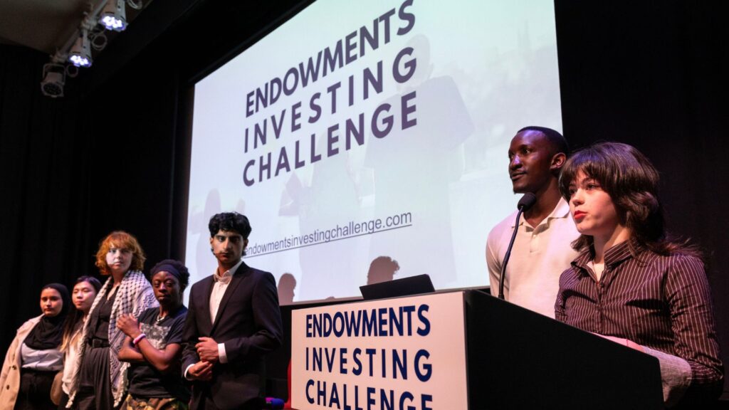 The Future Generations Panel on stage at the Endowments Investing Challenge event. Left to right - Viktoria, Lok-Yi, May, Jayden, Muhammed, Seth-Jesse and Izzy wo is peaking onto the microphone.